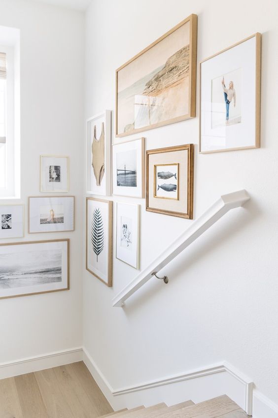 An airy gallery wall that takes up multiple walls and showcases beautiful art and photos with bright stained and white frames