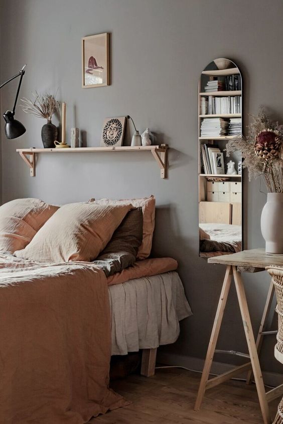 an earthy bedroom with gray walls, a bed with beige linens, a wooden console table, a mirror and a small shelf