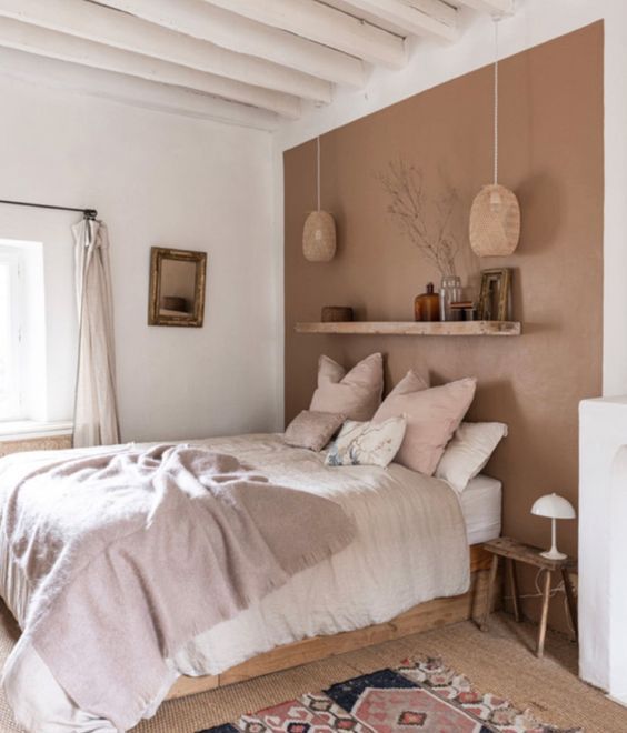 an earthy bedroom with a terracotta wall, a bed with neutral linens, a shelf with some decor and a bold printed rug