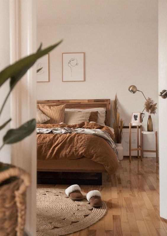 An earthy boho bedroom with a stained bed and rust colored linens, side tables, a jute rug and some artwork is amazing