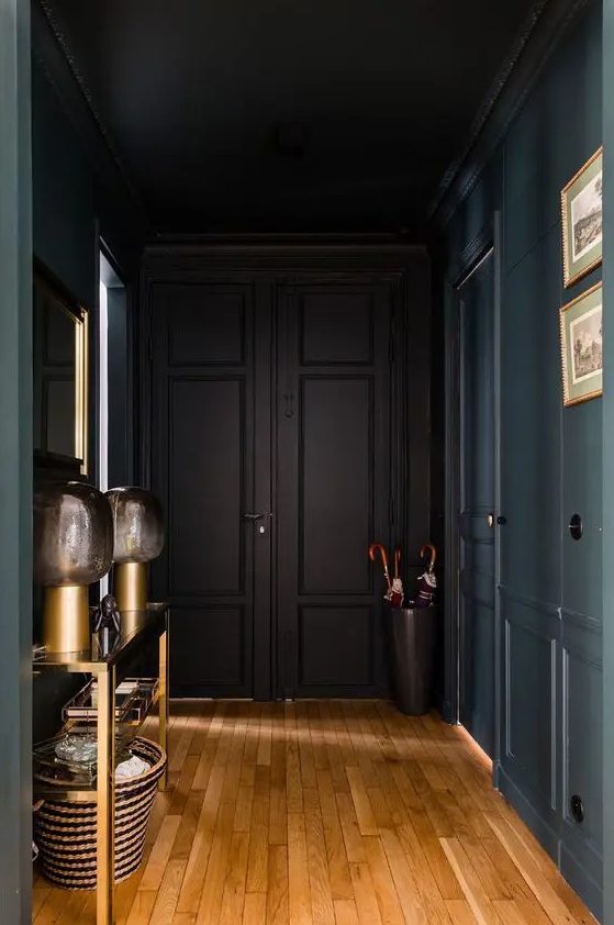 an elegant soot-colored entryway with a gold console table, table lamps, a basket, a bucket with umbrellas and artwork