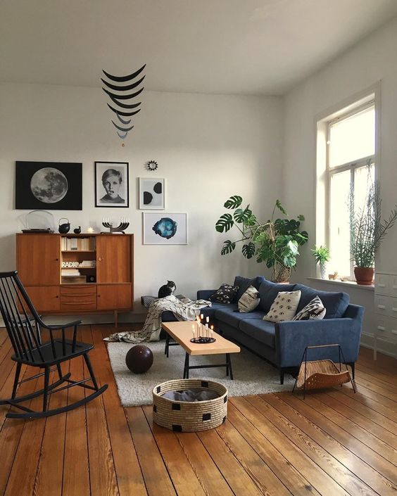 A mid-century modern living room with a navy blue sofa, a black rocking chair, potted plants, a stylish gallery wall and some cat furniture