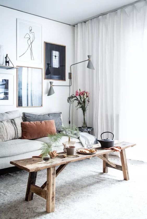 A Scandinavian living room is chic with a neutral sofa, a wooden bench, a beautiful gallery wall and gray sconces
