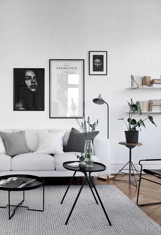 a laconic Scandi-style living room, with a white sofa, open shelves, black tables and a chair, black and white gallery wall