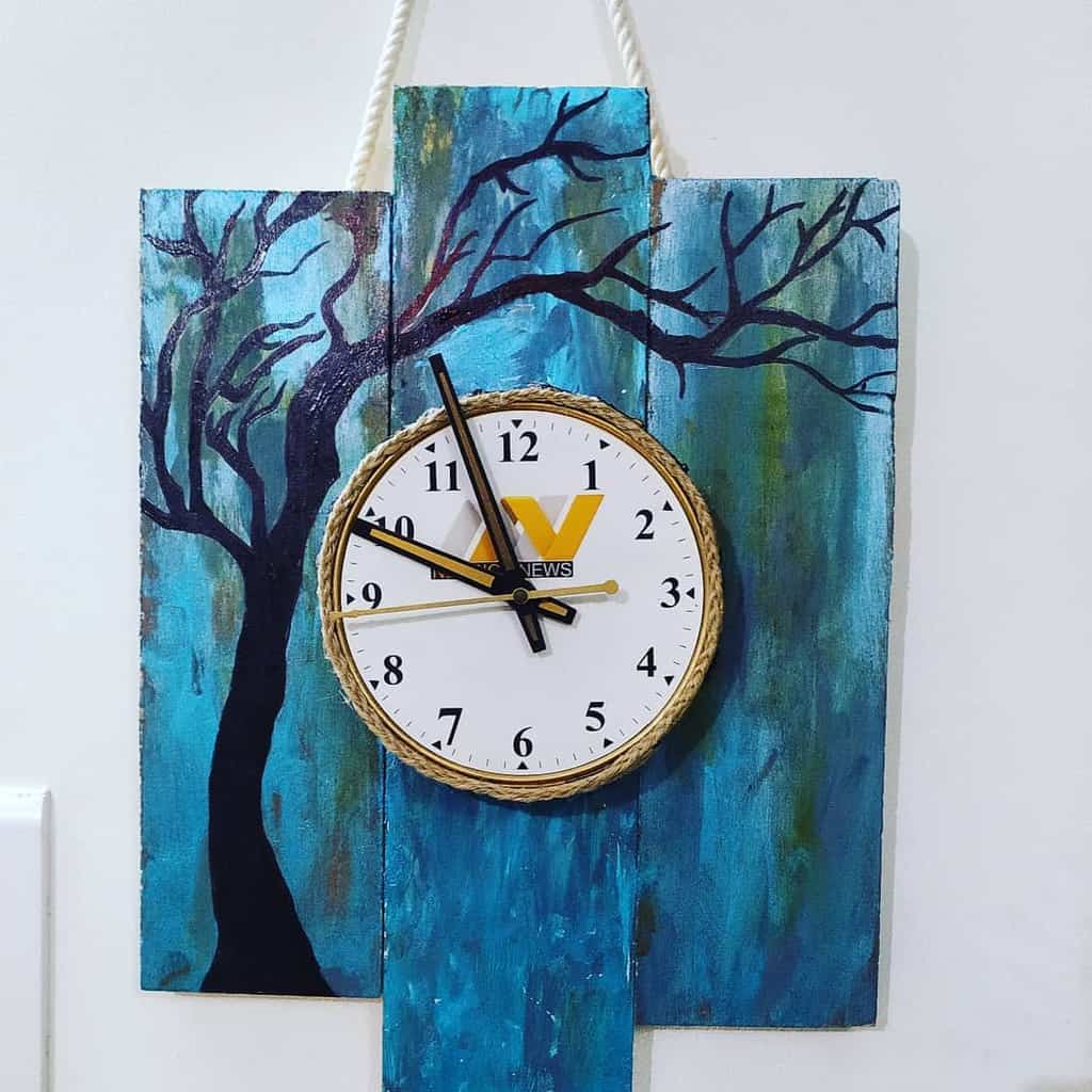 Clock on blue wooden planks with tree artwork 