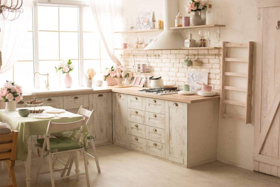Beige country kitchen, brick backsplash, ladder decoration, small dining table, green tablecloth