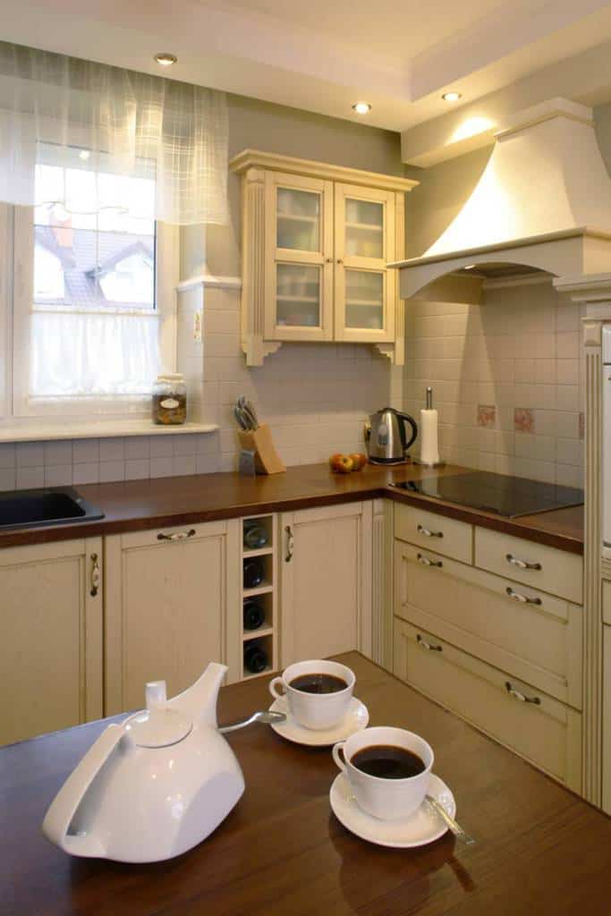 small corner kitchen, white cabinets, brown kitchen bench, teapot 
