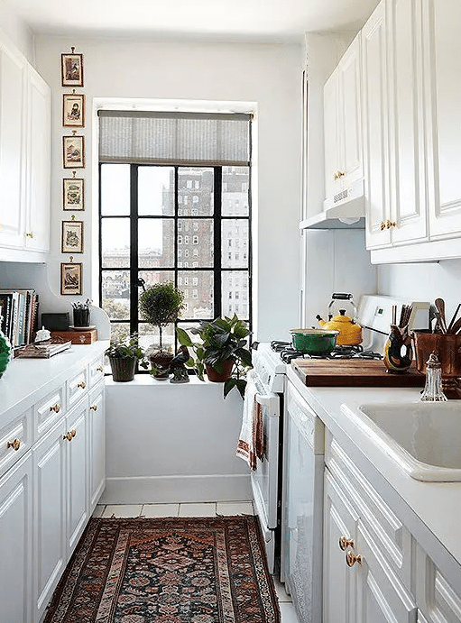 a cool galley kitchen with white cabinets, a boho rug, potted plants, a gallery wall and some bright accents