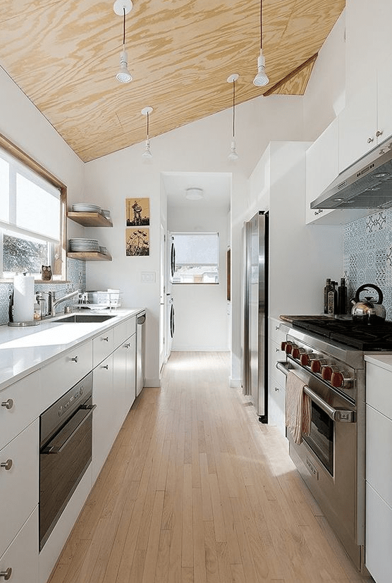 a modern white galley kitchen with a plywood ceiling with hanging lamps, a wooden floor and a blue tile backsplash