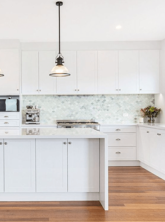 a serene white kitchen with shaker cabinets, a light gray, aquamarine and green fish scale tile backsplash, and white countertops