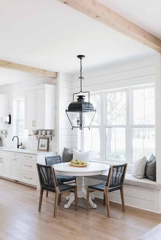 a stylish farmhouse kitchen with board walls and shaker cabinets, a windowsill bench and a round table and black chairs