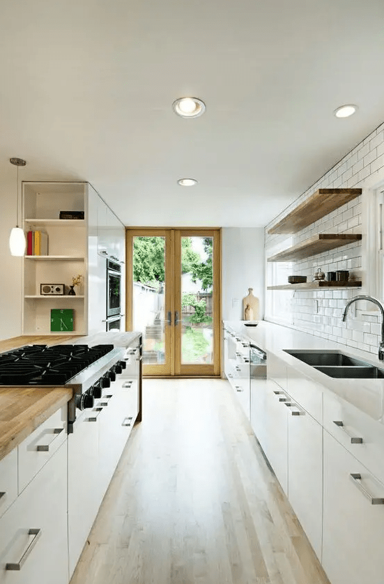 a white galley kitchen with a white subway tile backsplash, open shelving in place of upper cabinets and some lights