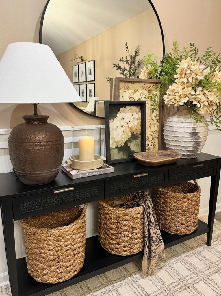 Black entrance table with round mirror, rattan baskets and floral decoration