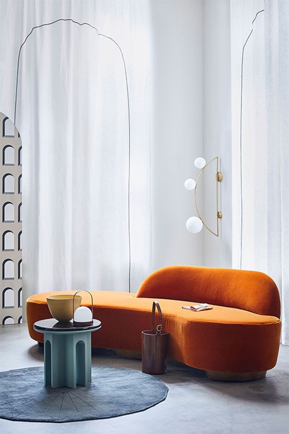 A bold, conceptual living room with a curved orange sofa, a round blue rug and a turquoise table for a bold interior