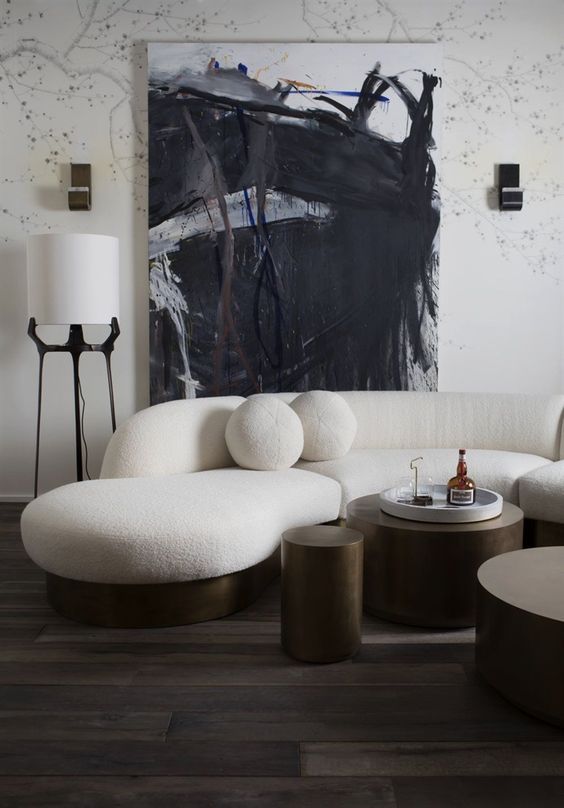 a monochrome living room with a cream curved sofa and round cushions and dark metal round tables