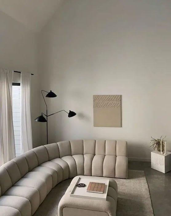 a beautiful warm colored neutral living room with a cream curved sofa and matching stool, a black floor lamp and a cube