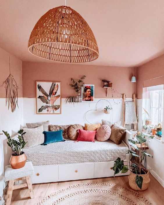 a boho room with a pink blanket, a daybed with pillows, a gallery wall, potted plants and a jute rug, as well as some decorations
