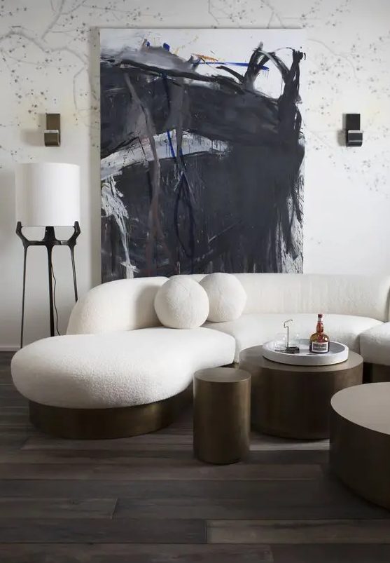 a bold and catchy living room with a white curved sofa with round cushions, metal tables, an abstract piece of art and some lamps