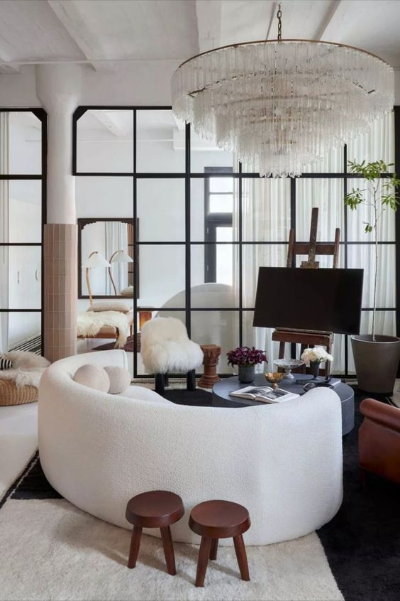 a bold living room with a white curved sofa, a gray round coffee table, a large and heavy crystal chandelier and some decor