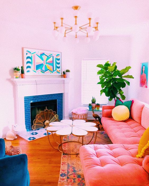 A bright living room with dopamine decor, a blue tile-lined fireplace, a peach pink sofa, light pillows, a coffee table and a navy blue chair