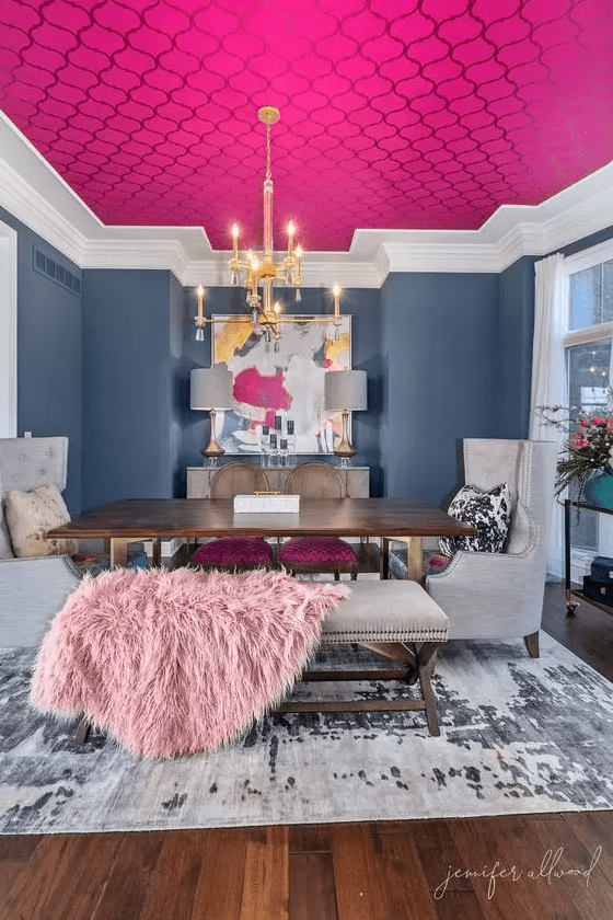 a bright, formal dining room with navy blue walls, a ceiling with pink printed wallpaper, a stained table and neutral chairs, and eye-catching artwork