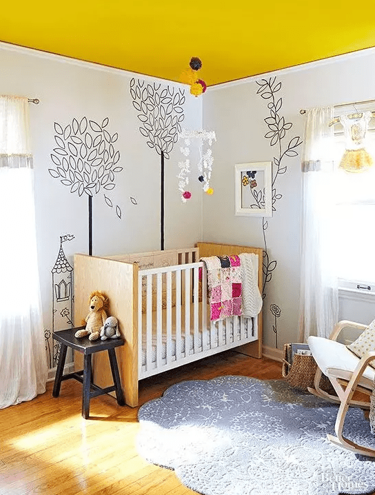 a bright children's room with a bright yellow ceiling, wall paintings, light stained furniture and a printed rug and some lovely toys