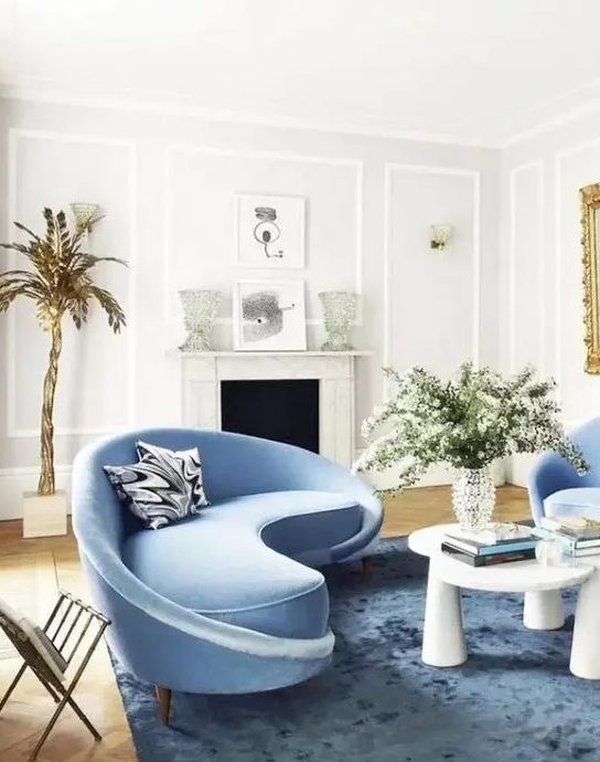 a charming living room with a curved blue sofa and matching chairs, as well as a statement table that catches the eye