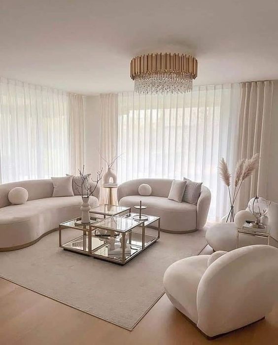 a chic, completely neutral living room with curved boucle furniture, coffee tables, a crystal chandelier and some decor