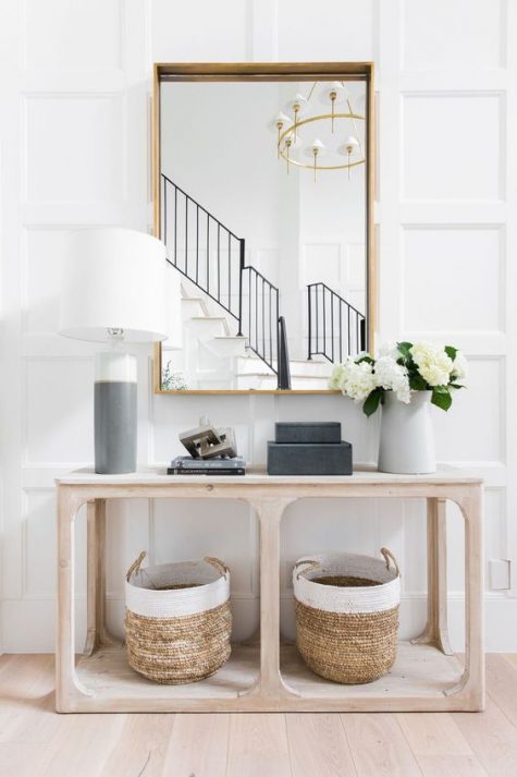 A chic, modern entryway with a large mirror, a pretty wooden console with baskets and a color-block lamp is simple and stylish