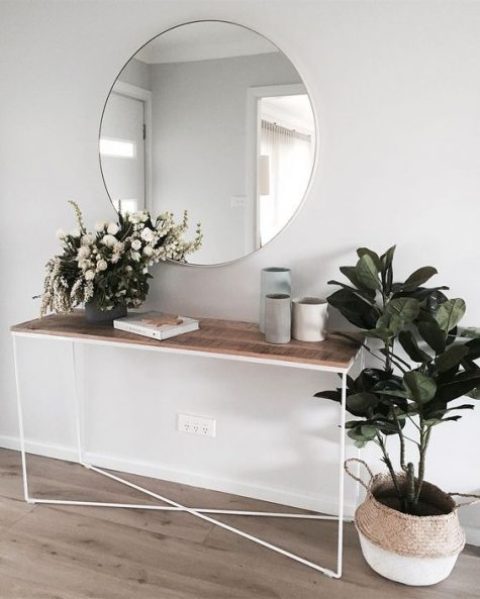 a chic, modern entryway with a wooden console, a round mirror and some potted plants and vases