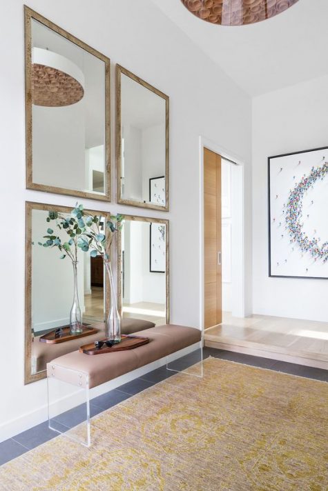 a chic, modern entryway with a gallery wall of mirrors, a leather and acrylic bench, and greenery in a vase