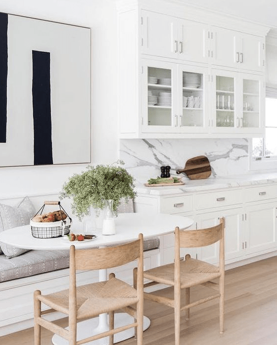 a chic white kitchen with a cozy dining area, a bench, wooden chairs and an oval table