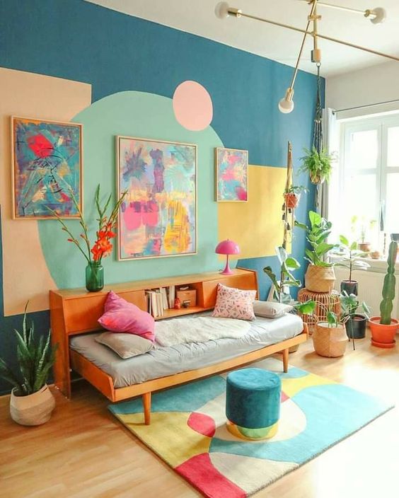 a colorful dopamine living room with a blue geo-print accent wall, a daybed with a bookcase, potted plants and bright artwork