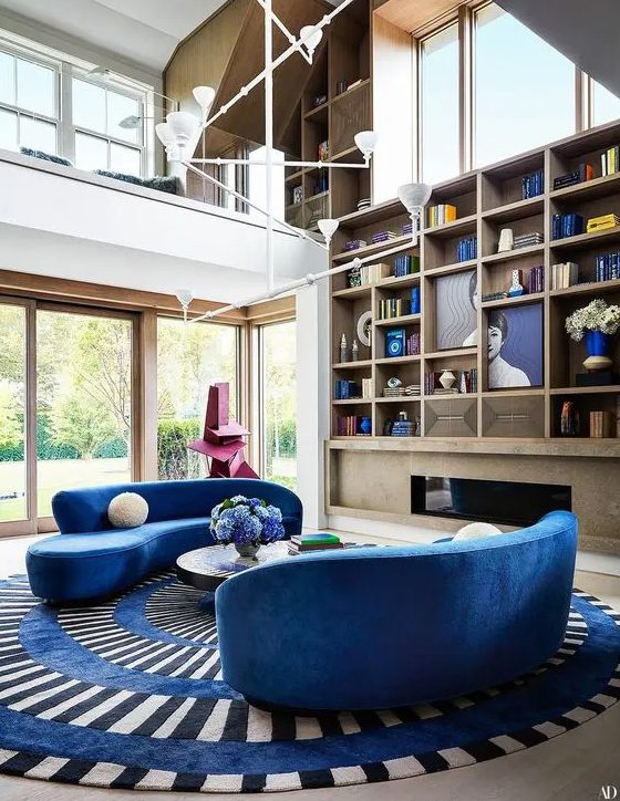 a colorful living room with a built-in fireplace, large built-in bookcase, bright blue curved sofas, a striped rug and a coffee table