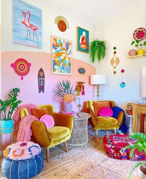 A colorful living room with dopamine decor, a pink accent wall, marigold chairs, colorful pillows and stools, and a statement gallery wall