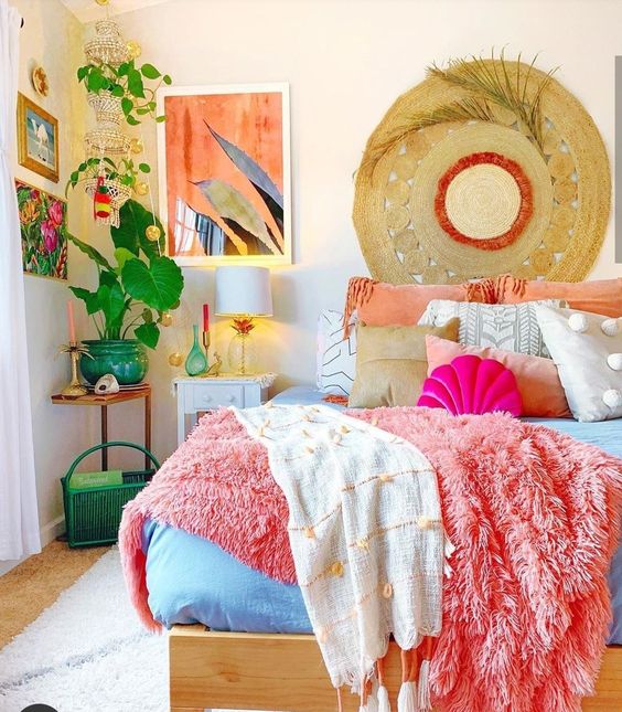 A bedroom in dopamine decor with a bed and striking coral and blue linens, a nightstand and corner table, eye-catching artwork and lots of greenery