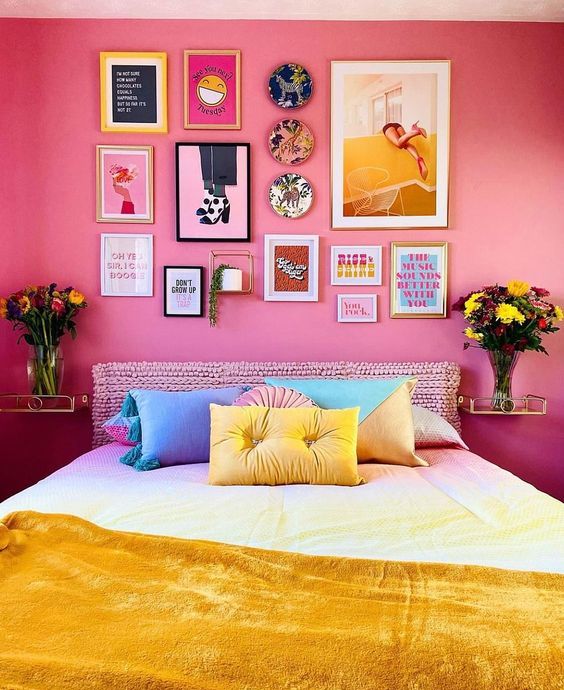 A bedroom in dopamine decor with bold pink walls, a bed with a knitted headboard, bright linens and a statement gallery wall