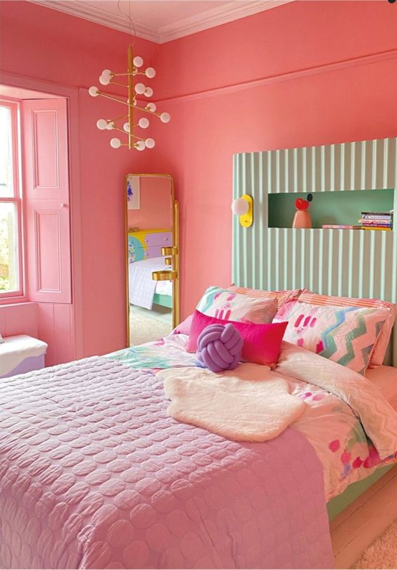 A bedroom in dopamine decor with coral walls and shutters, a bed with a mint green headboard, colorful and pastel linens and a mirror