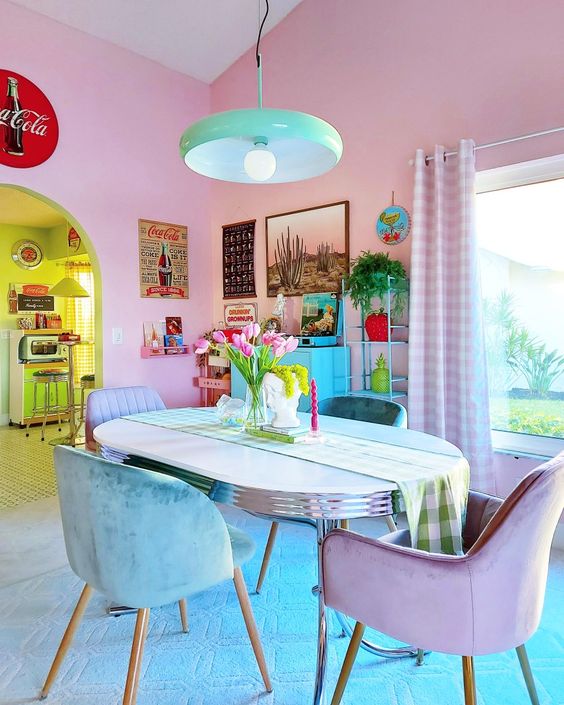 A dopamine decor dining room with blush walls, a turquoise and purple table and chairs, a statement gallery wall, and a green pendant lamp