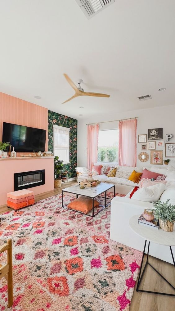 A living room in dopamine decor with peach fuzz accents, floral wallpaper, a white sofa, printed pillows and a bold printed rug
