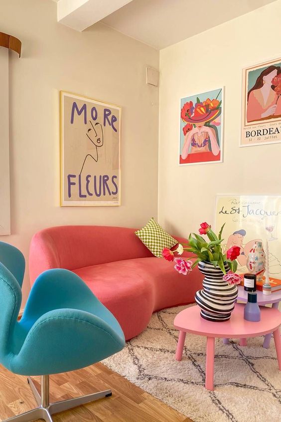 A dopamine decor living room with a coral curved sofa, blue chair, pink coffee table, eye-catching artwork and some decor