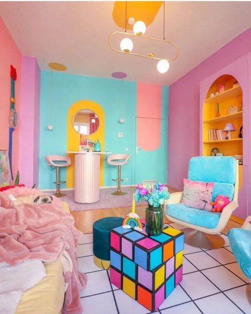 A living room in dopamine decor with pink, coral and turquoise walls, a sofa, pink blankets, a blue chair and a fun coffee table