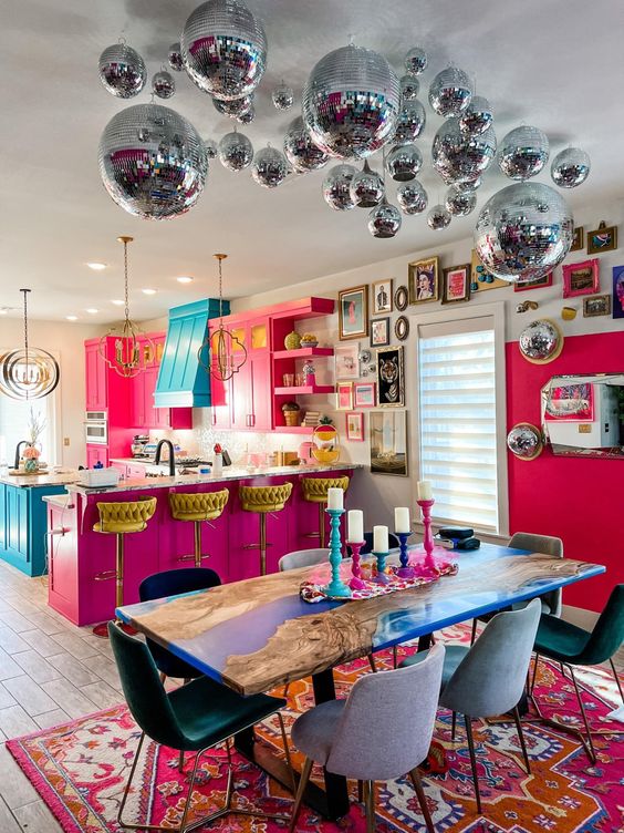 A dopamine decor area with a pink kitchen, turquoise range hood and kitchen island, bright blue table and disco balls above