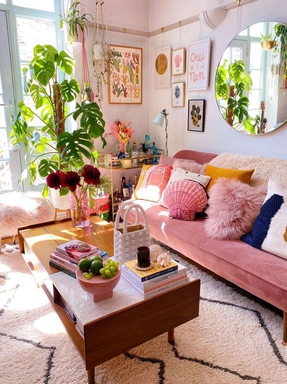 a dopamine decor with a pink sofa and colorful pillows, a coffee table, some plants and a gallery wall