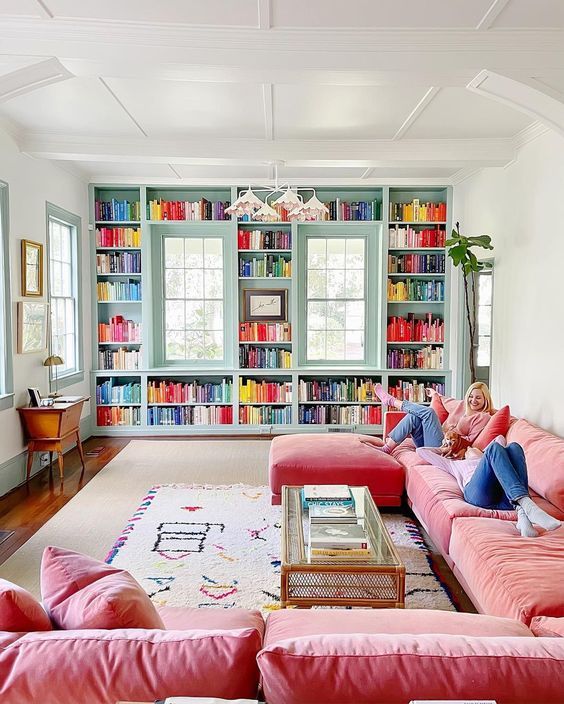 a dopamine living room with an aqua blue wall with bookshelves and colorful pillows, a large pink sofa, layered rugs and lots of greenery
