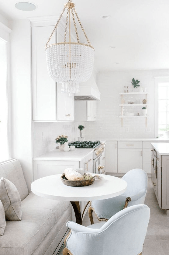 a glamorous white farmhouse kitchen with a gray island and a dining area with a love seat and blue chairs