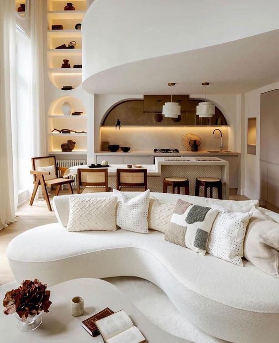 A beautiful neutral sophisticated space with a white curved bouclé sofa, coffee table, dining area and kitchen and niches with decor