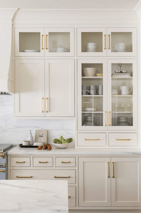 a beautiful cream kitchen with shaker and glass cabinets, white marble countertops and a splashback and gold handles