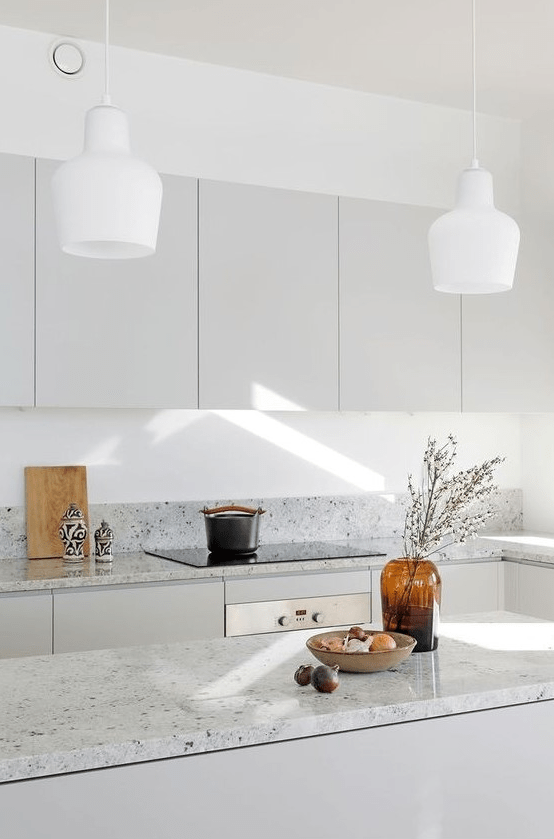 A minimalist gray kitchen with gray terrazzo countertops and white pendant lamps is a chic and inviting space