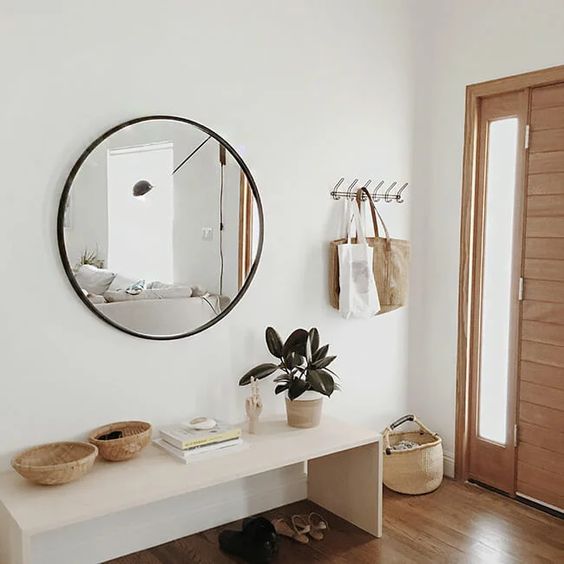 A modern entryway with an elegant bench, a round mirror, some baskets and a clothes rack is stylish and looks ethereal